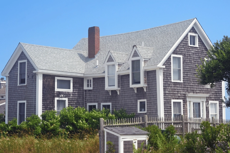 cape cod home with a brick chimney and fence surrounding the property